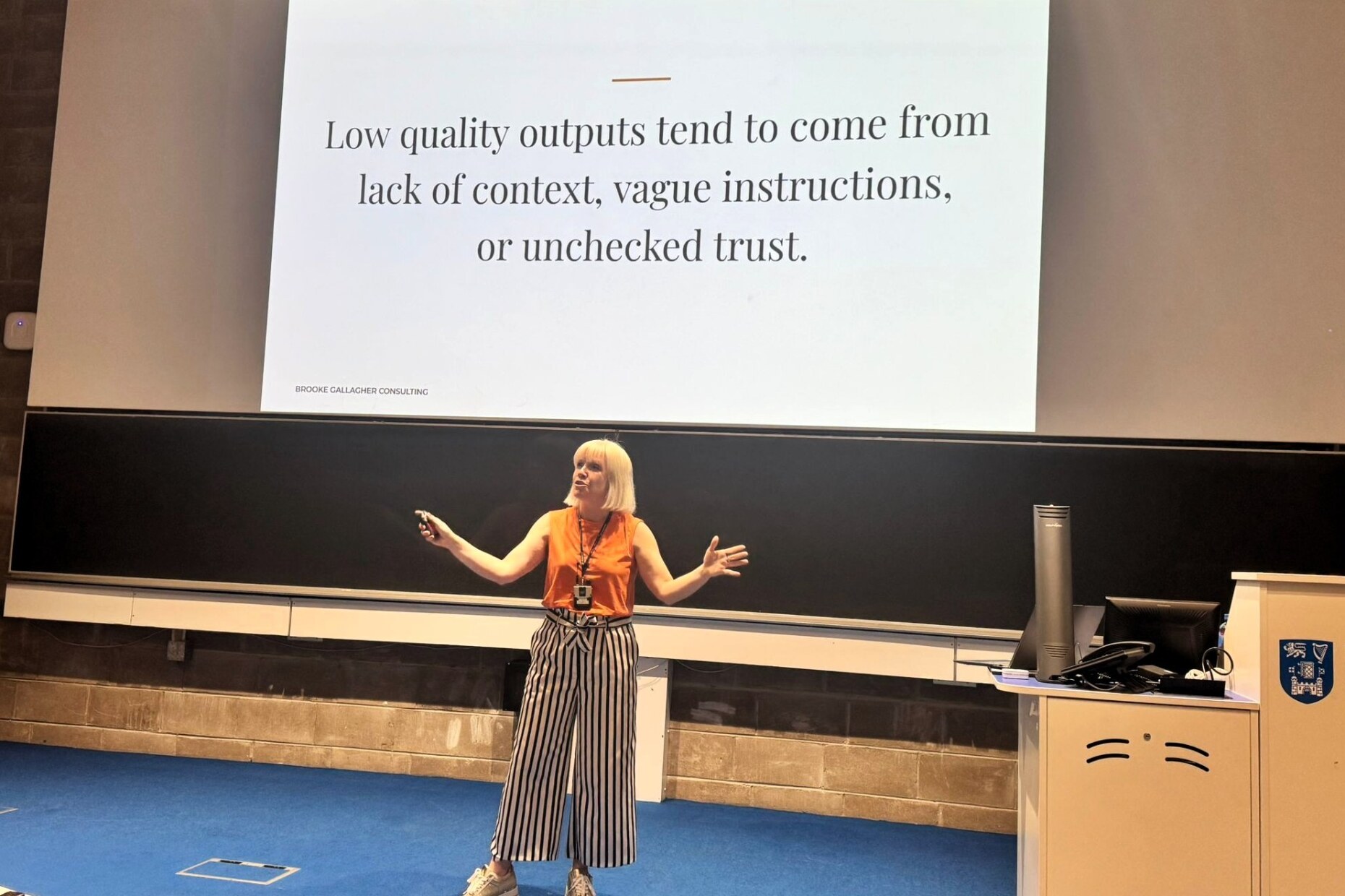Brooke Gallagher presenting at Trinity College Dublin, beside a slide reading ‘Low quality outputs tend to come from lack of context, vague instructions, or unchecked trust.’